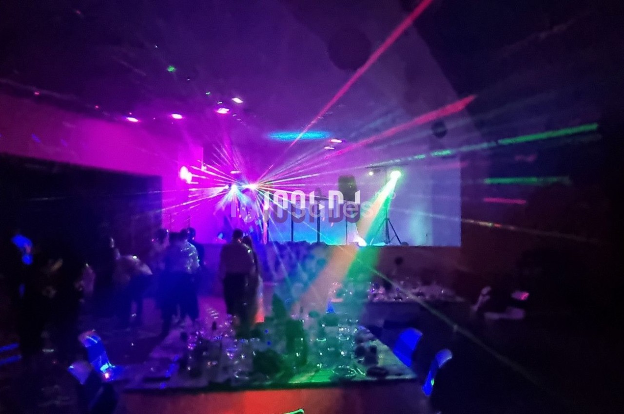 Salle sombre avec des jeux de lumière colorés, des personnes dansant et des tables dressées au premier plan.