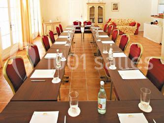 Salle de réunion lumineuse avec tables en U, chaises rouges, documents, bouteilles d'eau et verres disposés.