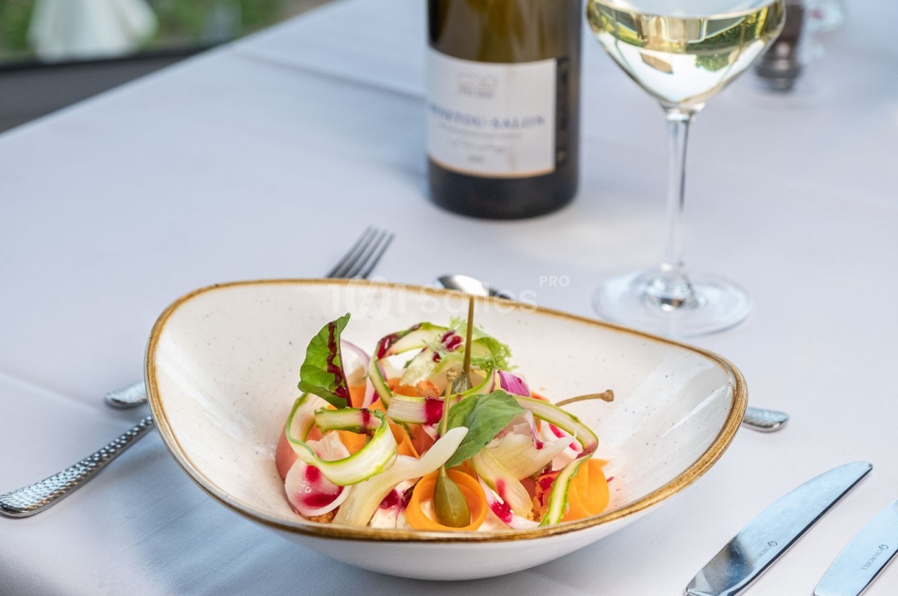 Assiette de salade colorée avec légumes frais, servie sur une table dressée avec un verre de vin blanc et une bouteille.