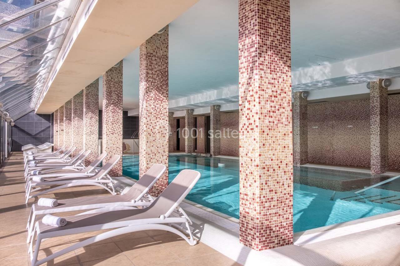 Piscine intérieure avec colonnes décoratives et chaises longues alignées sur un sol carrelé.
