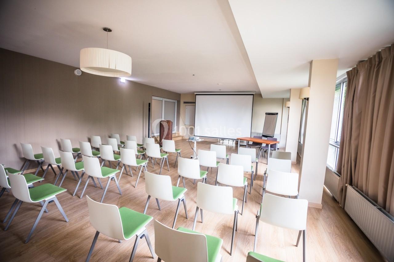Salle de réunion lumineuse avec des rangées de chaises blanches et vertes, un écran de projection et un tableau de…