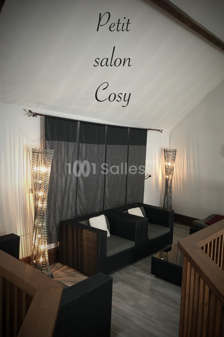 Espace salon avec deux canapés en rotin, coussins blancs, lampes décoratives et rideaux gris dans une ambiance cosy.