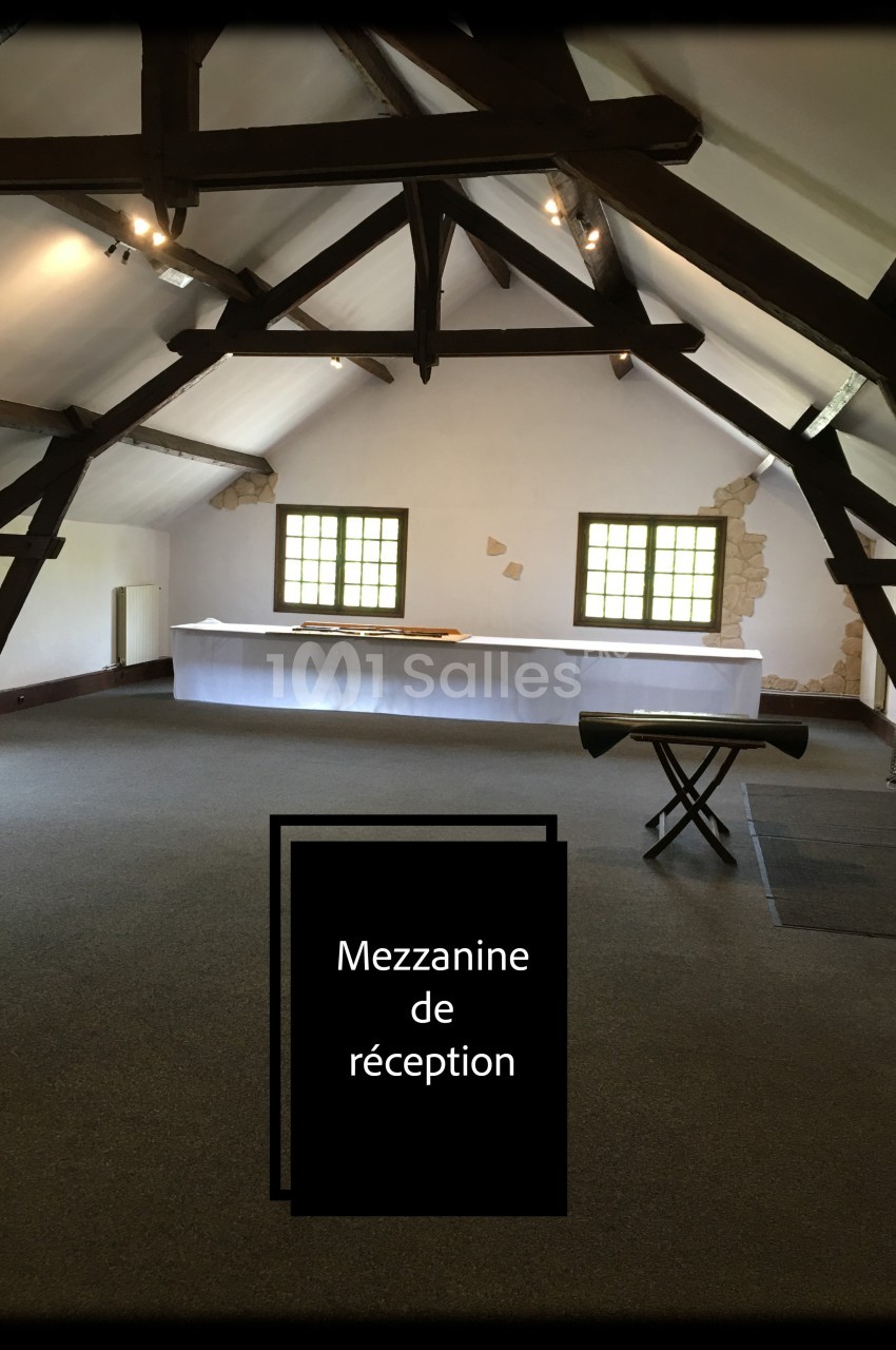 Salle de réception avec poutres apparentes, grandes fenêtres et une table recouverte d'une nappe blanche.