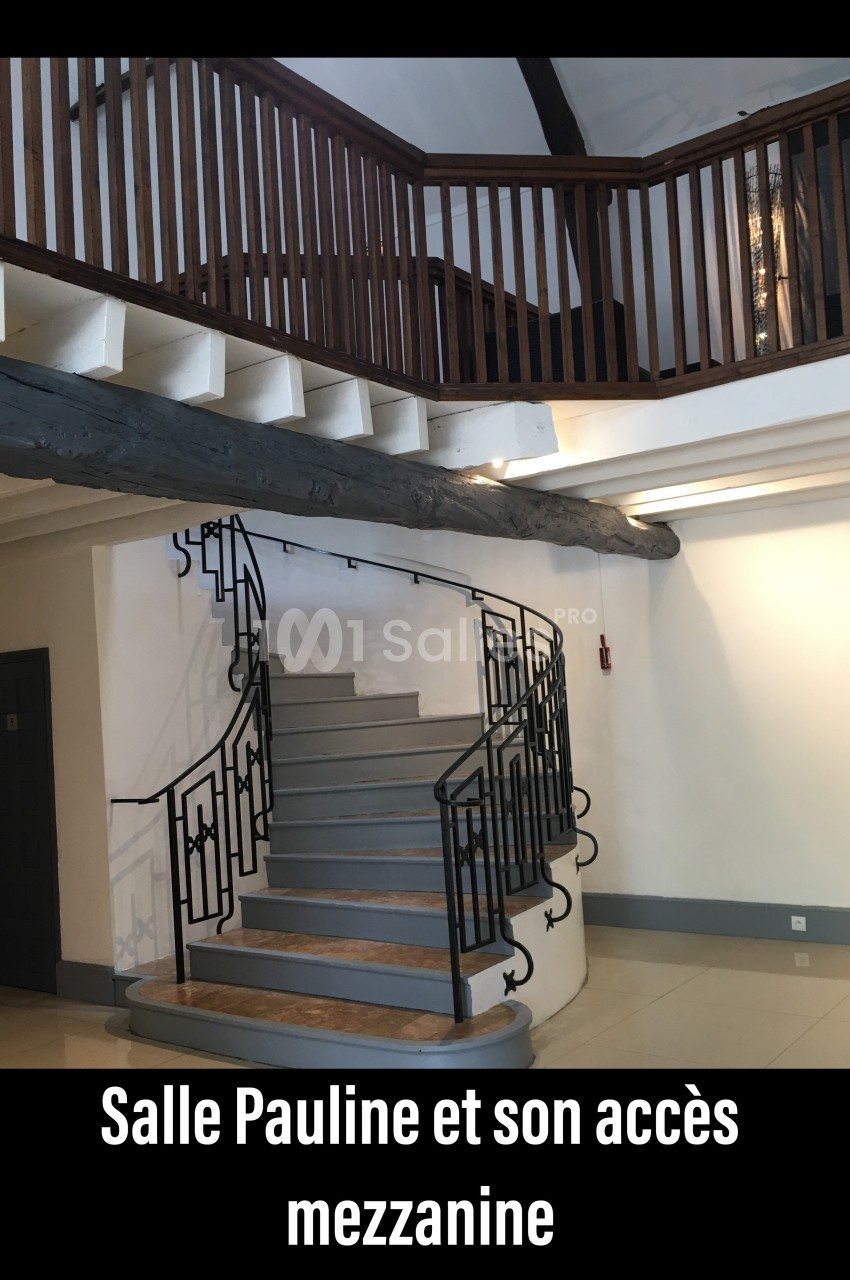 Escalier en colimaçon avec garde-corps en métal menant à une mezzanine en bois dans une salle lumineuse.
