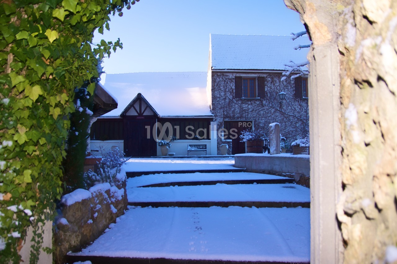 Cour enneigée entourée de murs en pierre, avec une maison en arrière-plan sous un ciel dégagé.