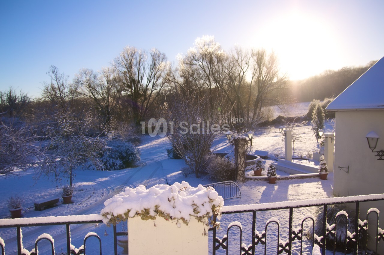 Paysage hivernal avec jardin enneigé, arbres dénudés et soleil bas illuminant la scène.