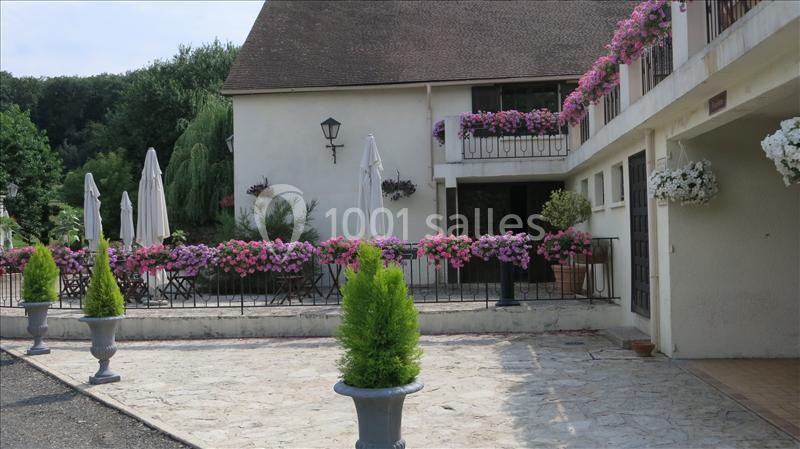 Cour pavée avec terrasse fleurie, parasols blancs et façade de maison ornée de jardinières colorées.