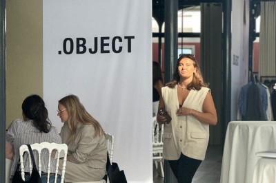 Espace lumineux avec tables hautes, affiches de mode et personnes discutant sous une structure métallique.