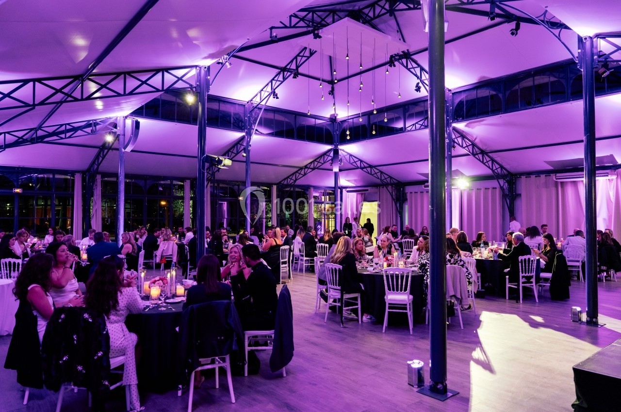 Salle de réception lumineuse avec des invités assis à des tables rondes sous un éclairage violet.
