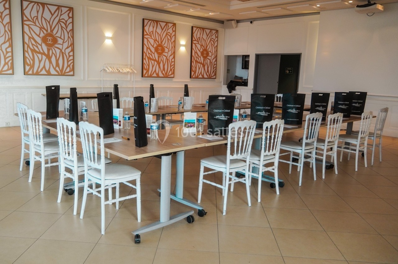 Salle de réunion aménagée avec des tables en bois, des chaises blanches, des sacs cadeaux et des bouteilles d'eau.
