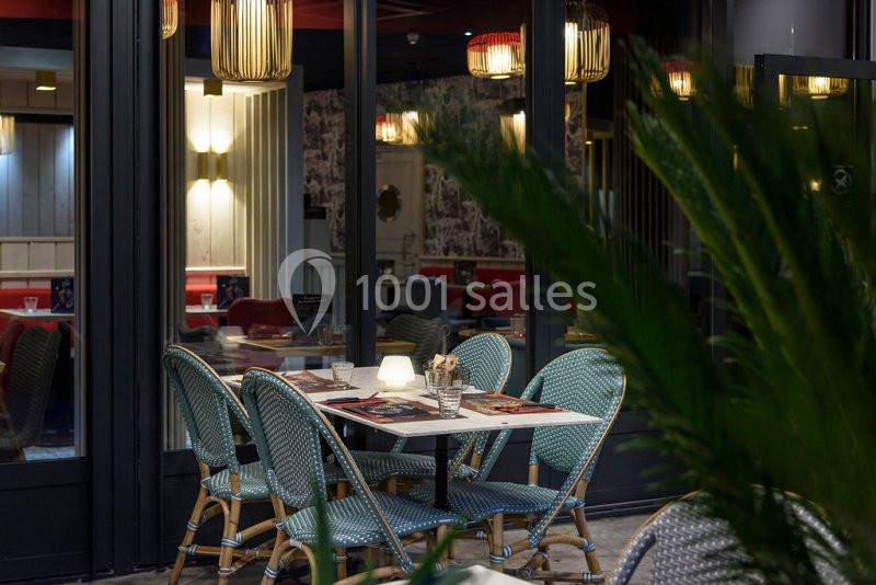 Table de restaurant en terrasse avec chaises en osier, éclairage tamisé et vue sur l'intérieur décoré.