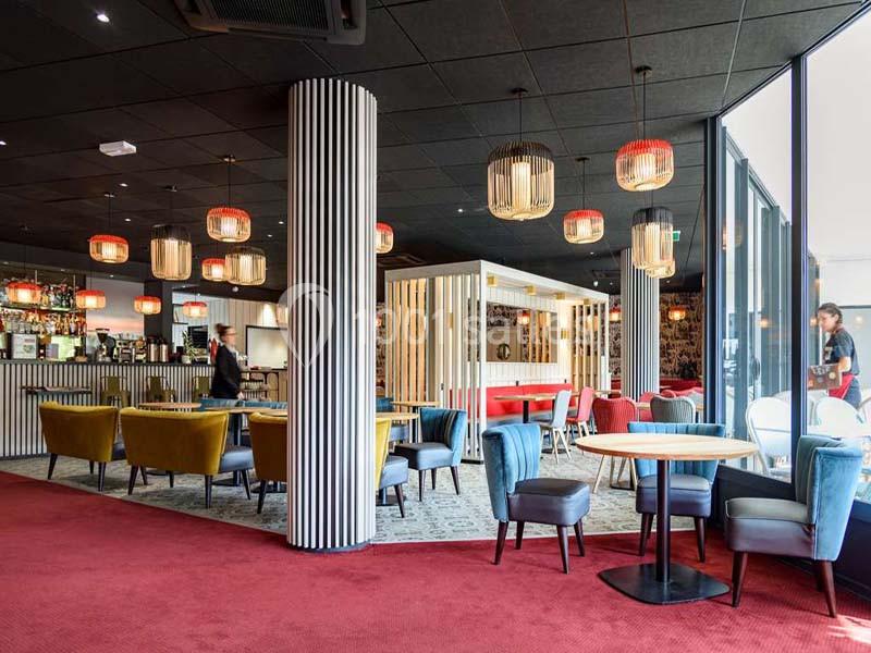 Salle de restaurant moderne avec mobilier coloré, luminaires suspendus et grandes baies vitrées.