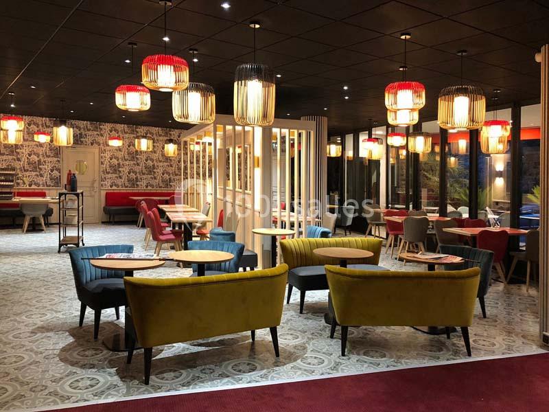 Salle de restaurant moderne avec fauteuils colorés, tables en bois, luminaires suspendus et décorations murales.