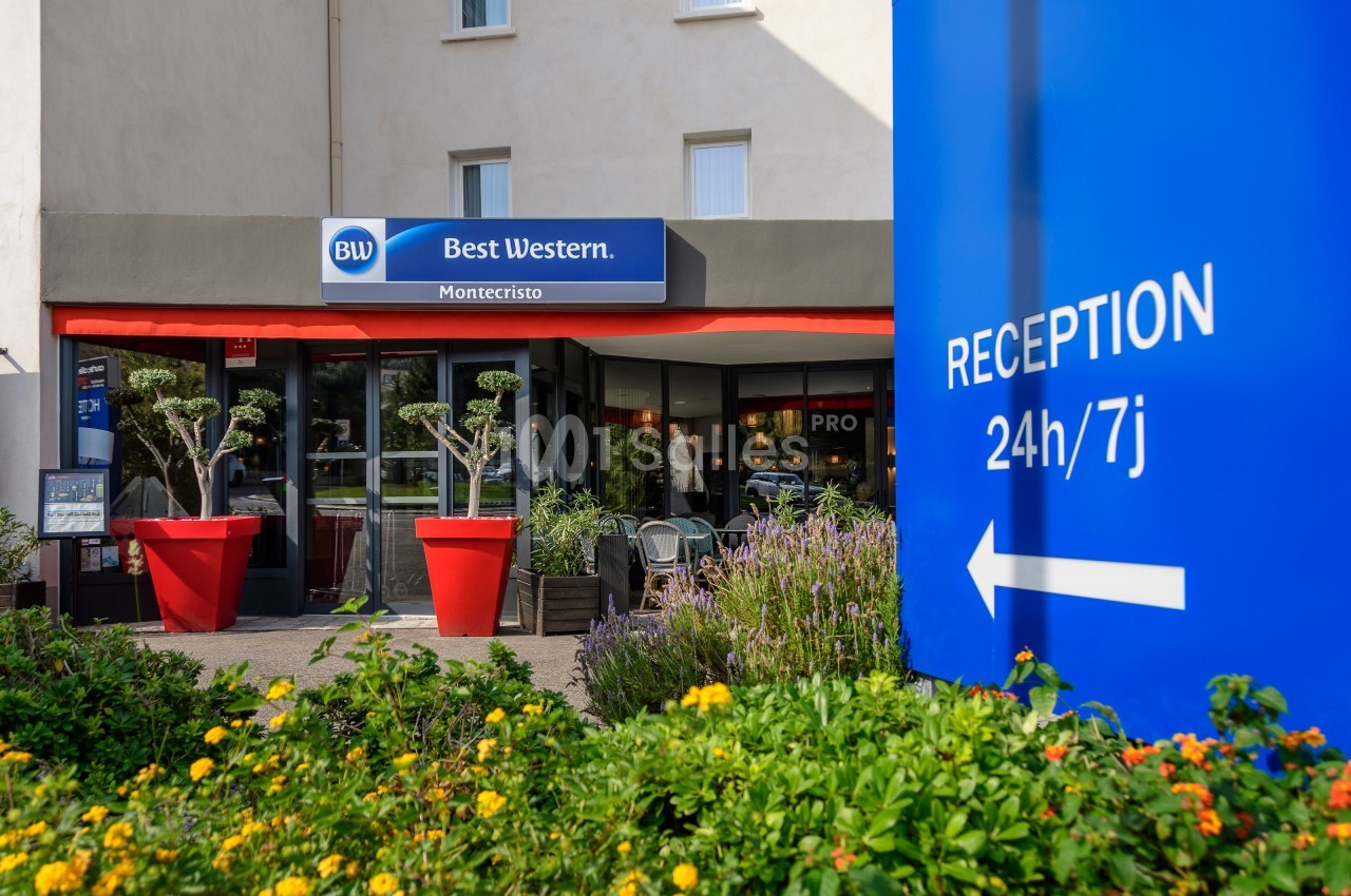 Façade d'un hôtel Best Western avec entrée principale, plantes en pot et panneau indiquant une réception ouverte 24h/7j.