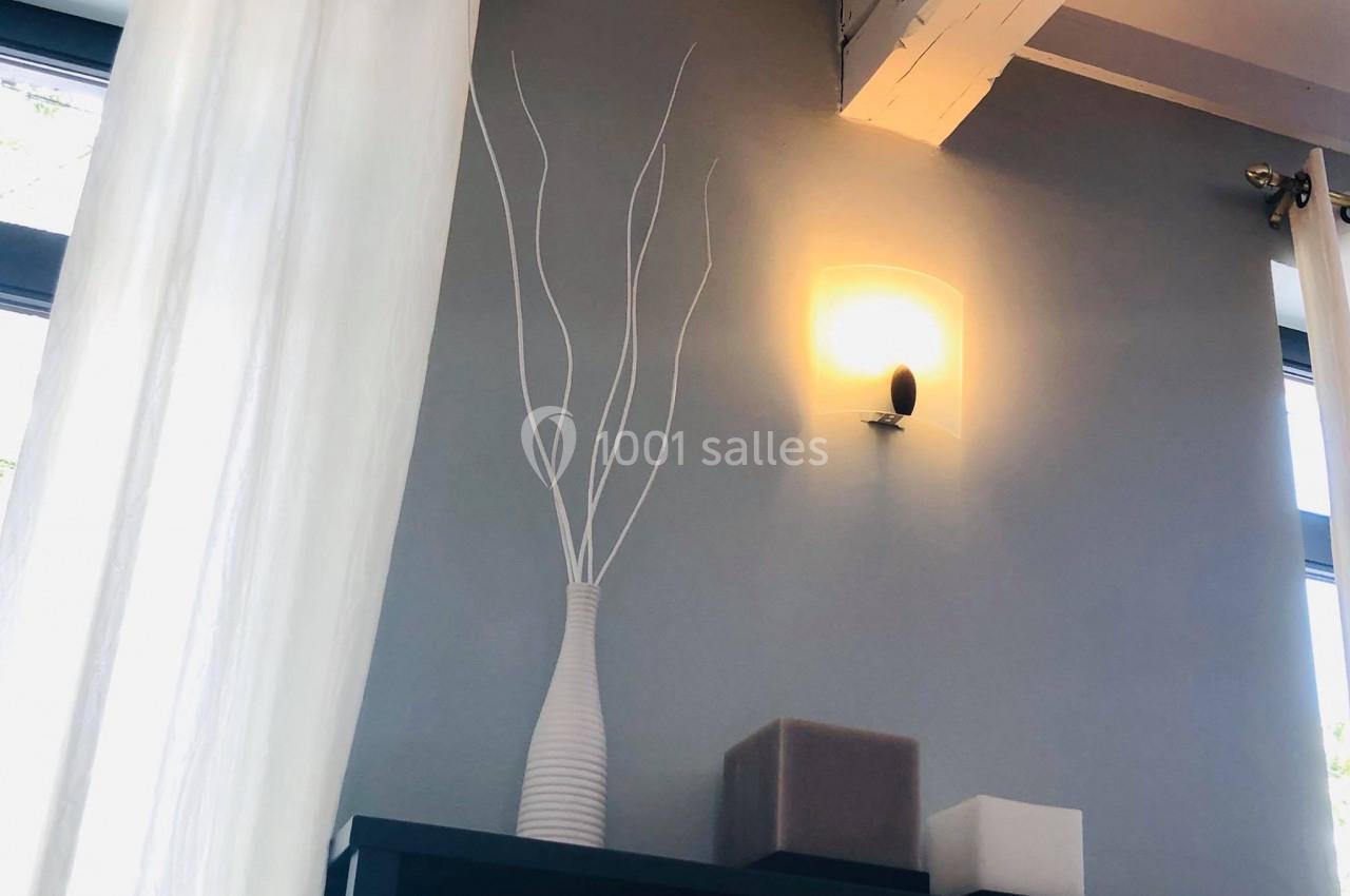Location salle Mouscron (Hainaut) - Le Belvédère #13 Vase blanc avec branches décoratives posé sur un meuble noir, éclairé par une applique murale sur fond de mur gris.