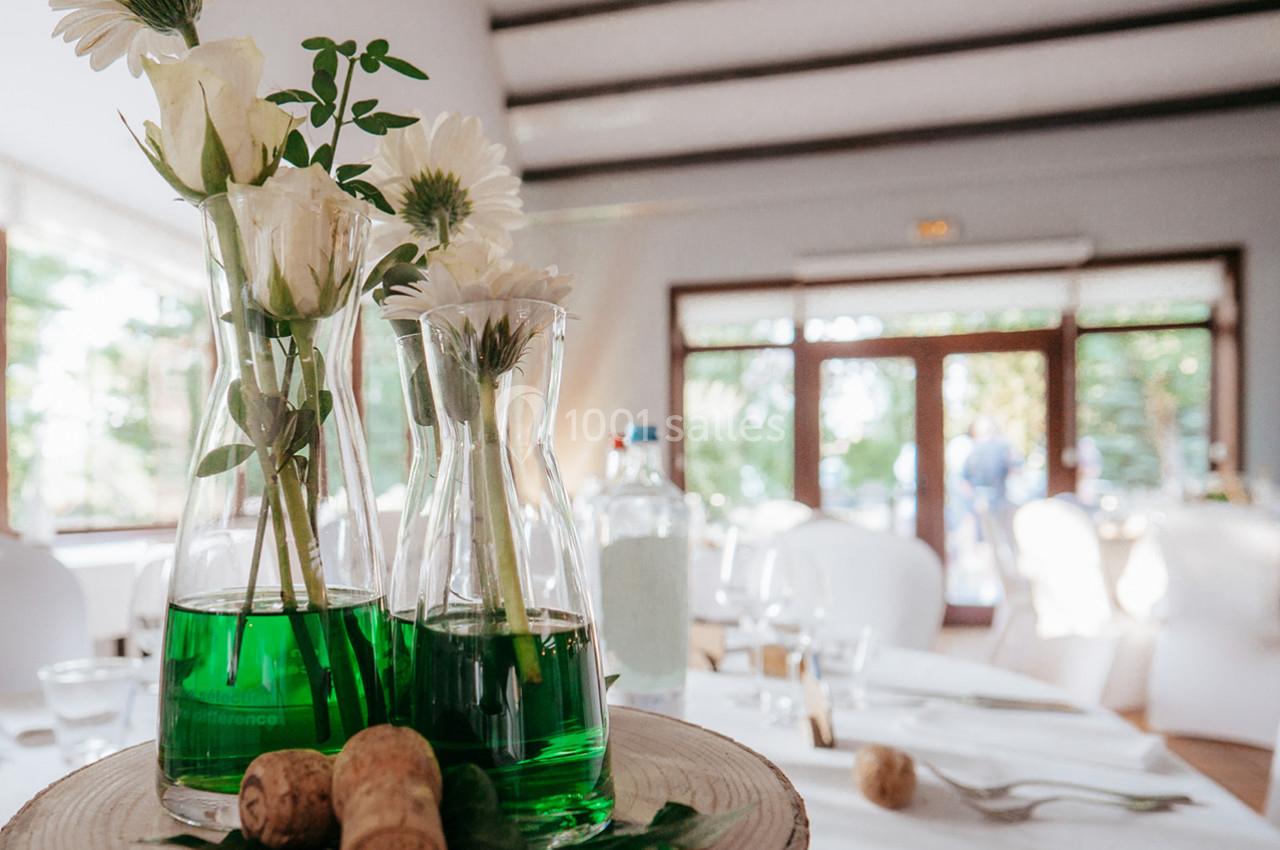 Location salle Mouscron (Hainaut) - Le Belvédère #10 Vases en verre contenant des fleurs blanches et un liquide vert, posés sur une rondelle de bois dans une salle lumineuse.