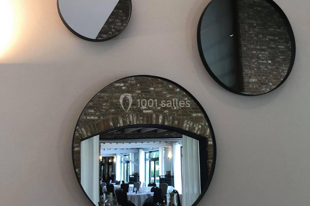 Location salle Mouscron (Hainaut) - Le Belvédère #12 Trois miroirs ronds accrochés sur un mur beige, reflétant une salle lumineuse avec des tables dressées.