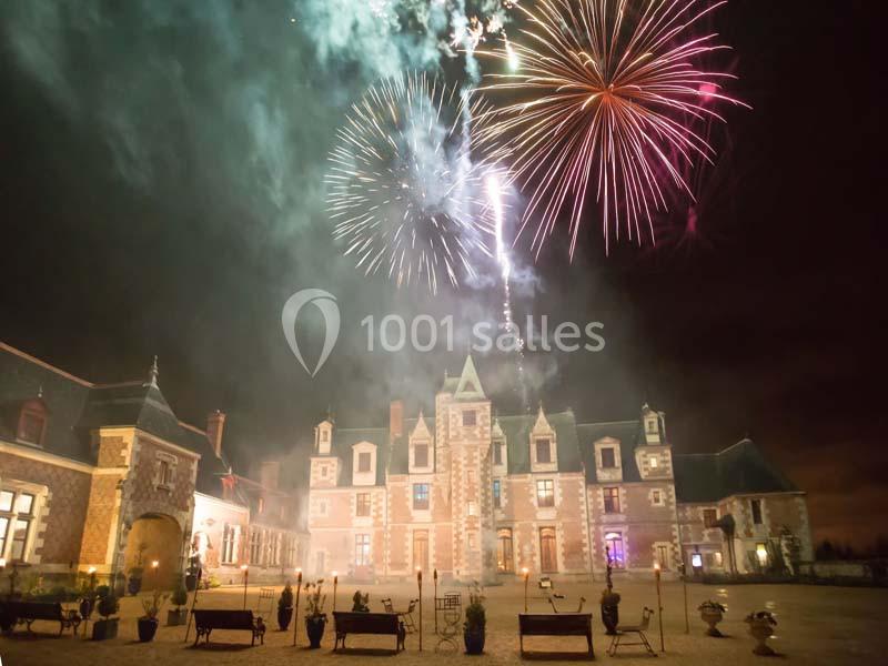 Feu d'artifice illuminant le ciel nocturne au-dessus d'un château en pierre avec une cour éclairée.