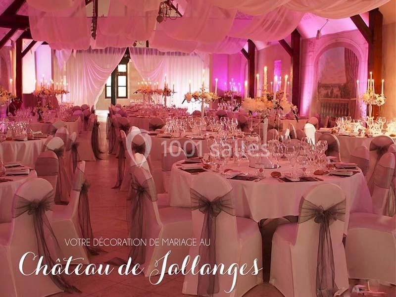 Salle de réception décorée pour un mariage avec tables dressées, chaises ornées de rubans et éclairage rose.