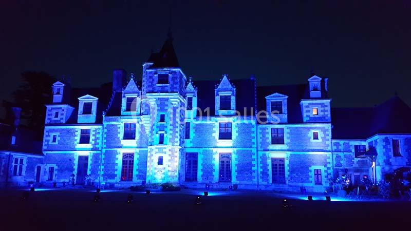 Façade d'un château illuminée en bleu dans l'obscurité, avec des fenêtres et des détails architecturaux visibles.