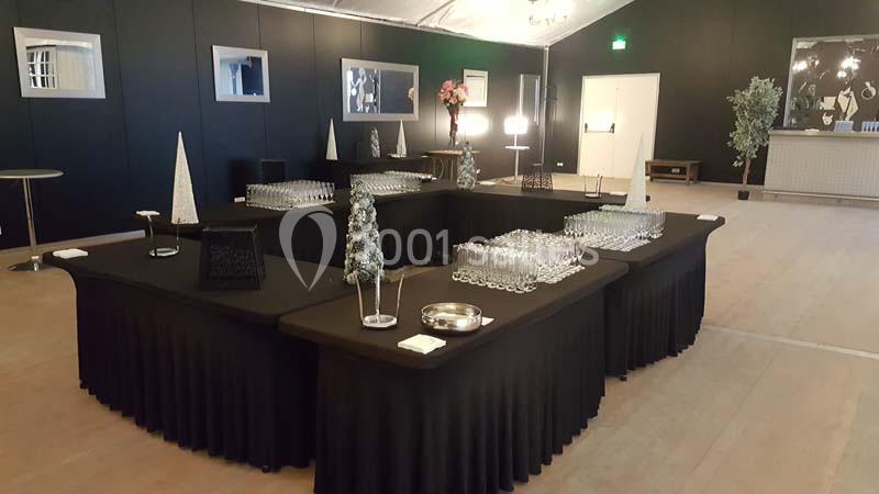 Tables noires disposées en U avec des verres alignés, décorations minimalistes et éclairage intérieur tamisé.