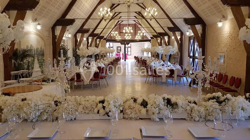 Salle de réception décorée avec des tables dressées, des chaises rouges et des arrangements floraux blancs.