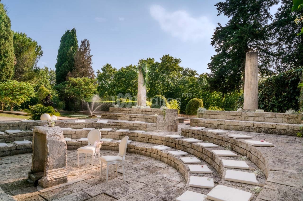 Amphithéâtre en pierre entouré de verdure, avec des chaises blanches et des coussins disposés sur les gradins.
