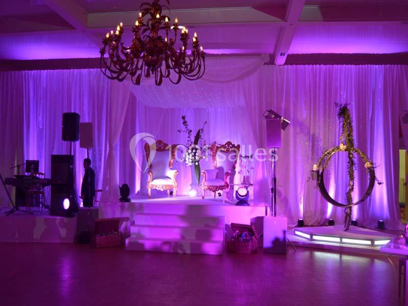Salle de réception décorée avec des rideaux blancs, éclairages violets, fauteuils dorés et un lustre central.