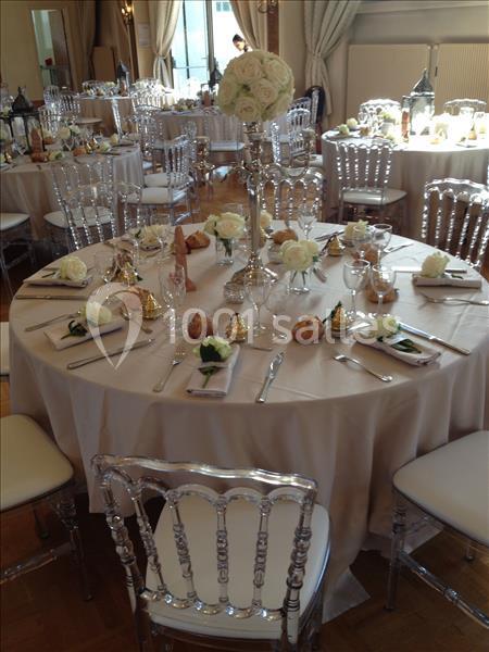 Table de réception élégamment dressée avec nappes blanches, chaises transparentes, fleurs et couverts disposés.