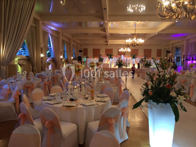 Salle de réception élégamment décorée avec tables rondes, chaises ornées de nœuds et éclairage chaleureux.