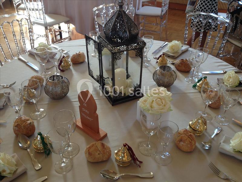 Table de réception décorée avec une lanterne centrale, des roses blanches, des bougies et des petits cadeaux dorés.