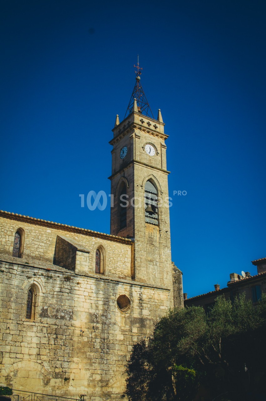 Clocher en pierre d'une église ancienne avec horloge, sous un ciel bleu clair.