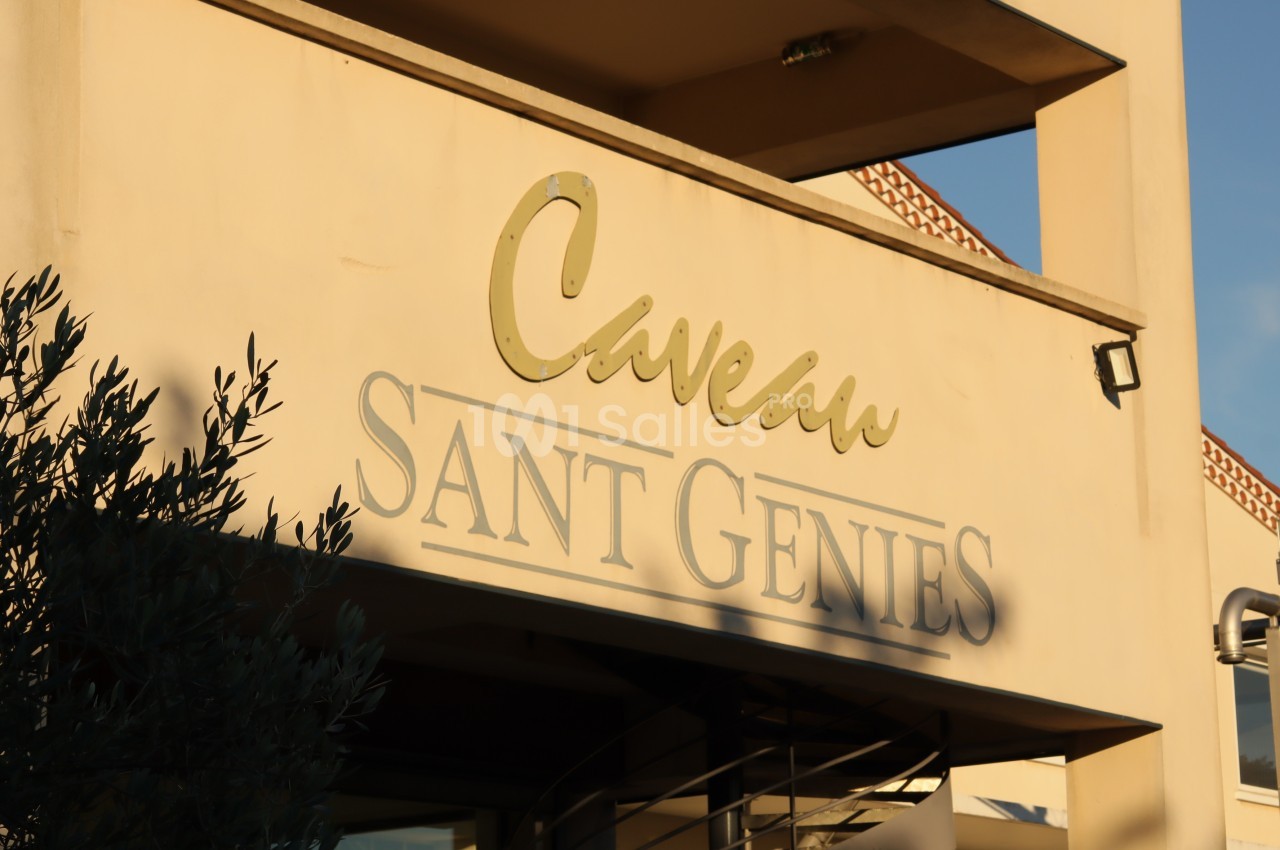 Façade d'un bâtiment beige avec l'inscription ’Caveau Sant Genies’ éclairée par la lumière du soleil.