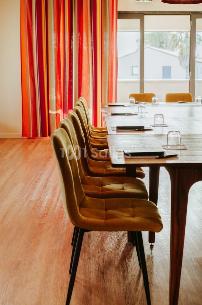 Chaises jaunes alignées le long d'une table en bois dans une salle lumineuse avec des rideaux rouges à rayures.