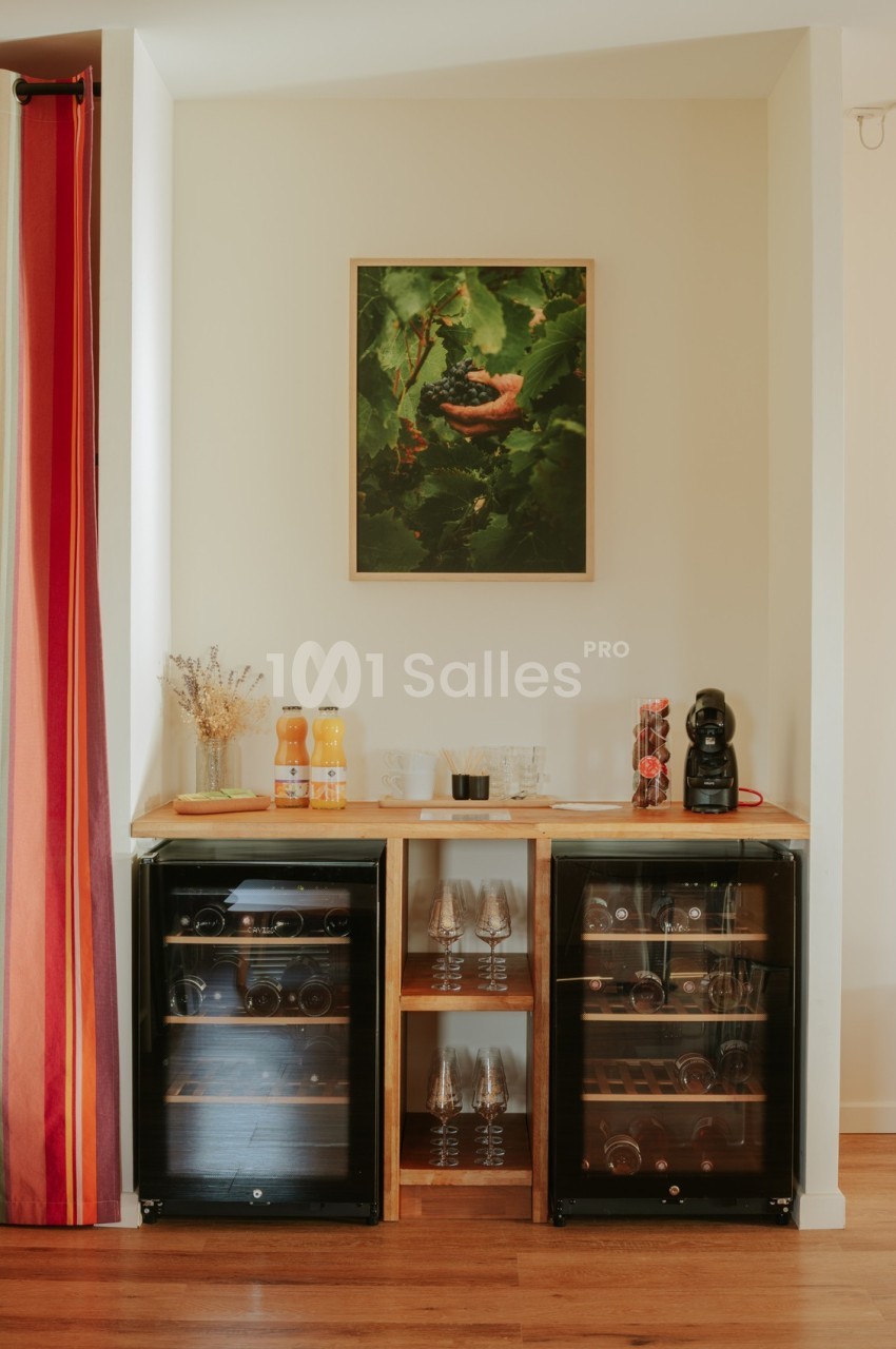 Meuble avec deux caves à vin, étagères de verres, boissons, machine à café et tableau décoratif au mur.
