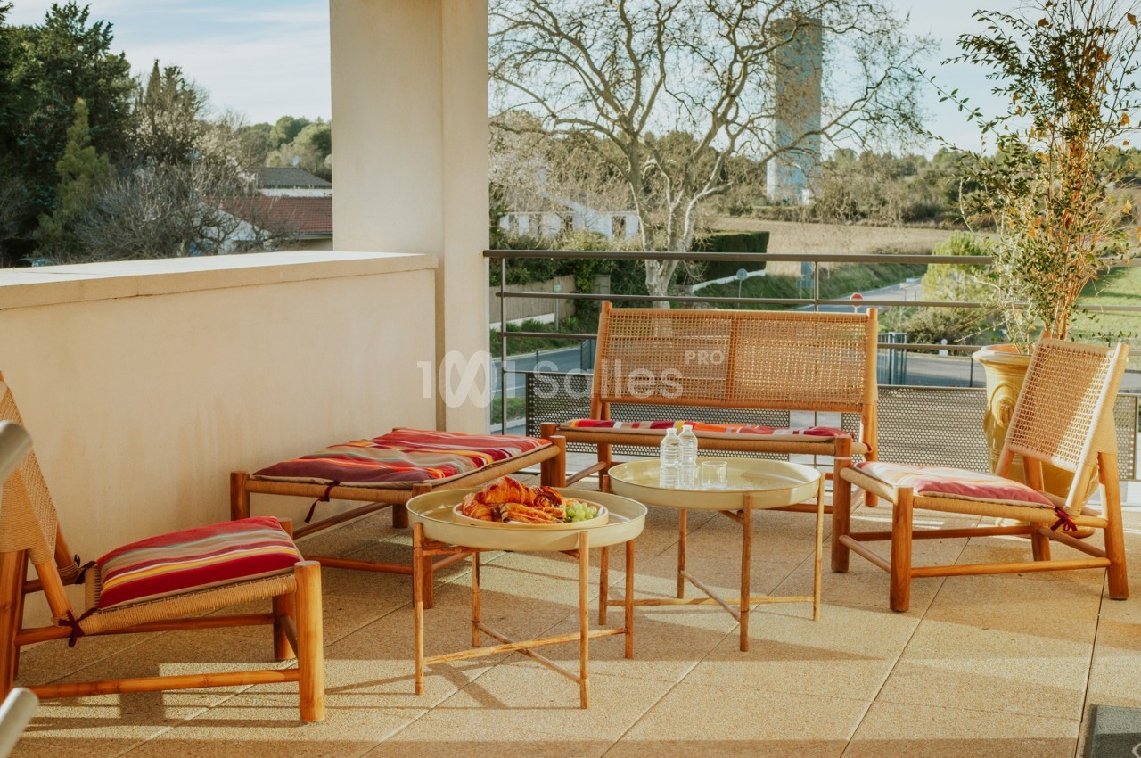 Terrasse ensoleillée avec mobilier en bois, coussins rayés rouges et table basse garnie de snacks et boissons.