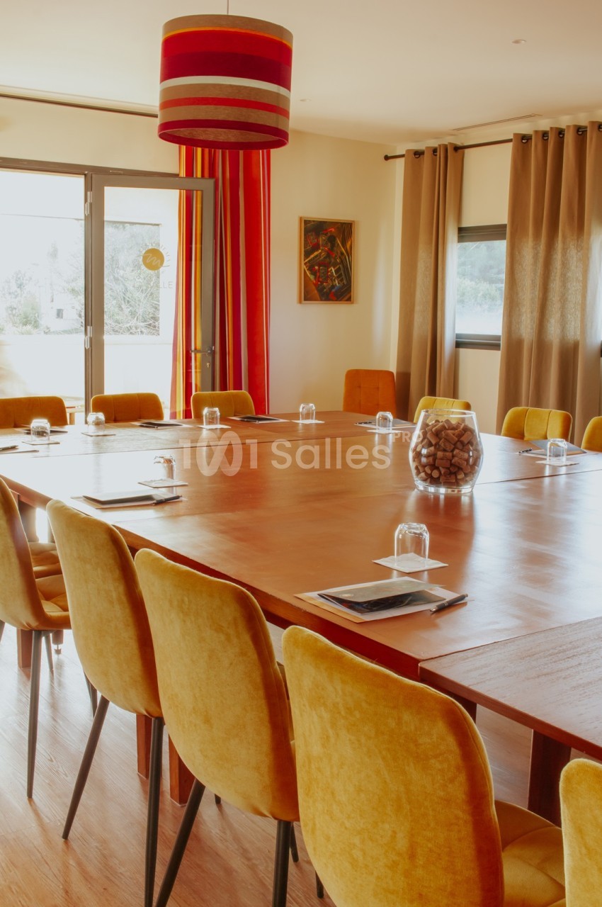 Salle de réunion lumineuse avec une grande table en bois, des chaises jaunes et une décoration chaleureuse.