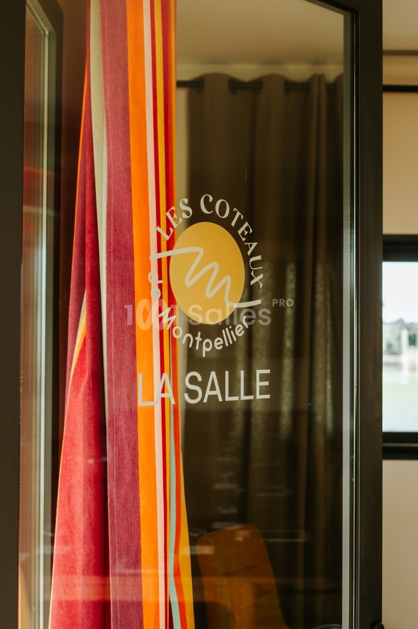 Porte vitrée avec logo ’Les Coteaux Montpellier’ et inscription ’La Salle’, rideaux colorés en arrière-plan.