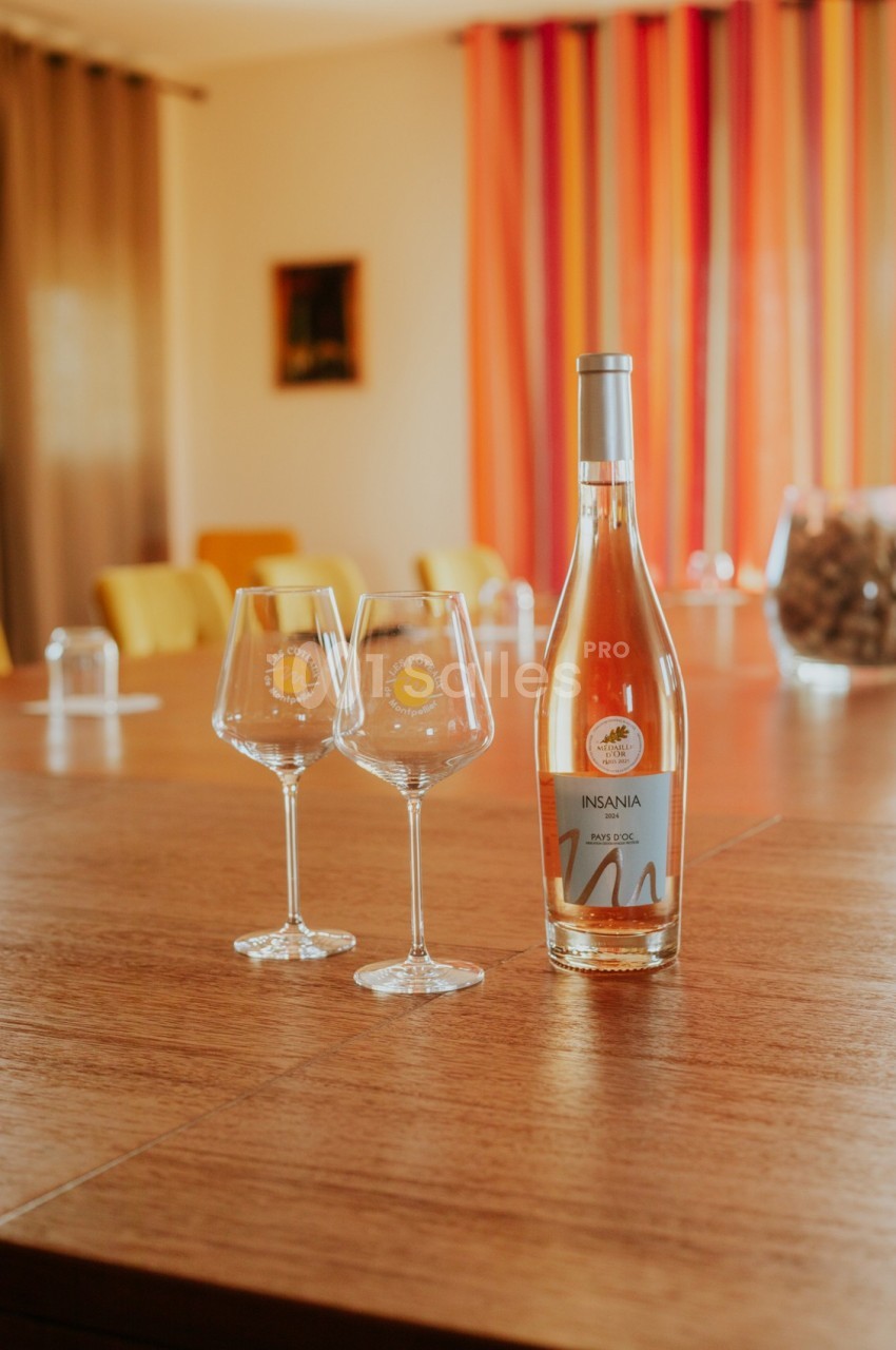 Bouteille de vin rosé et deux verres sur une table en bois, avec des rideaux colorés en arrière-plan.