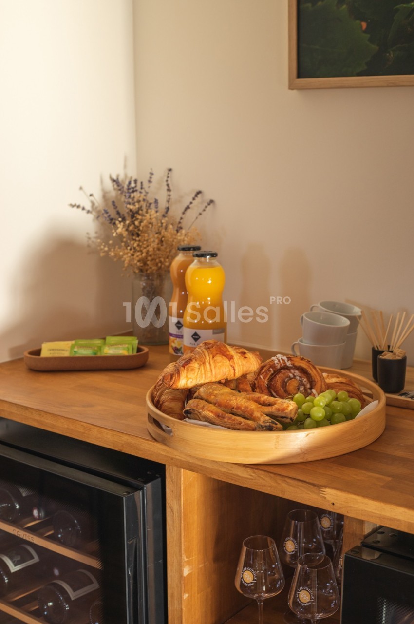 Plateau de viennoiseries, raisins et jus d'orange sur un buffet en bois avec décoration sobre et lumineuse.