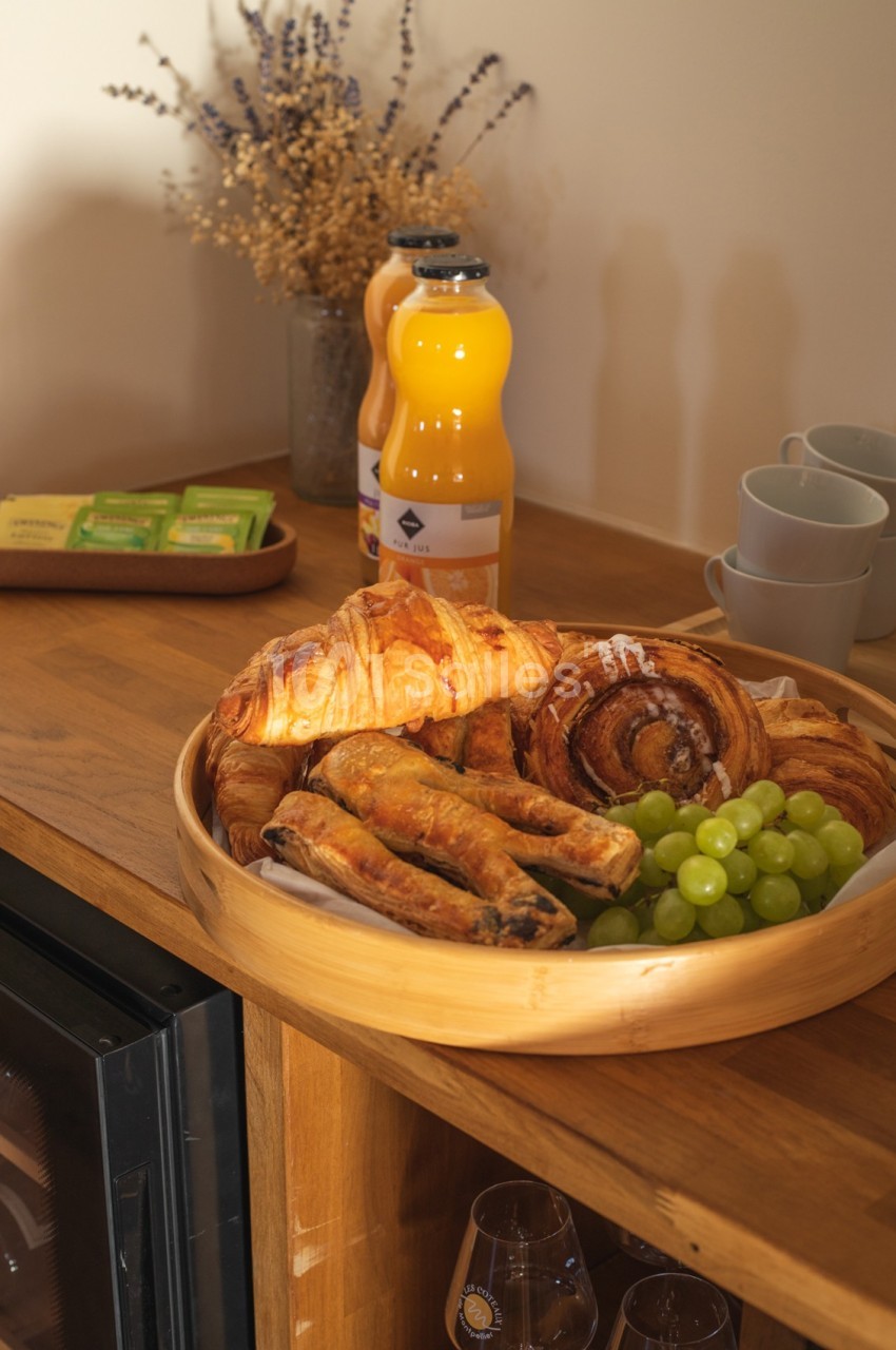 Plateau en bois avec viennoiseries, raisins verts, jus d'orange et tasses sur un comptoir en bois.