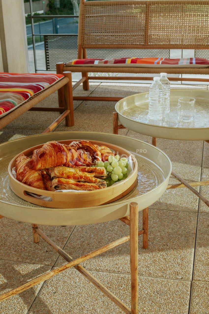 Plateau en bois avec croissants et raisins posé sur une table basse, entouré de mobilier en rotin sur une terrasse.