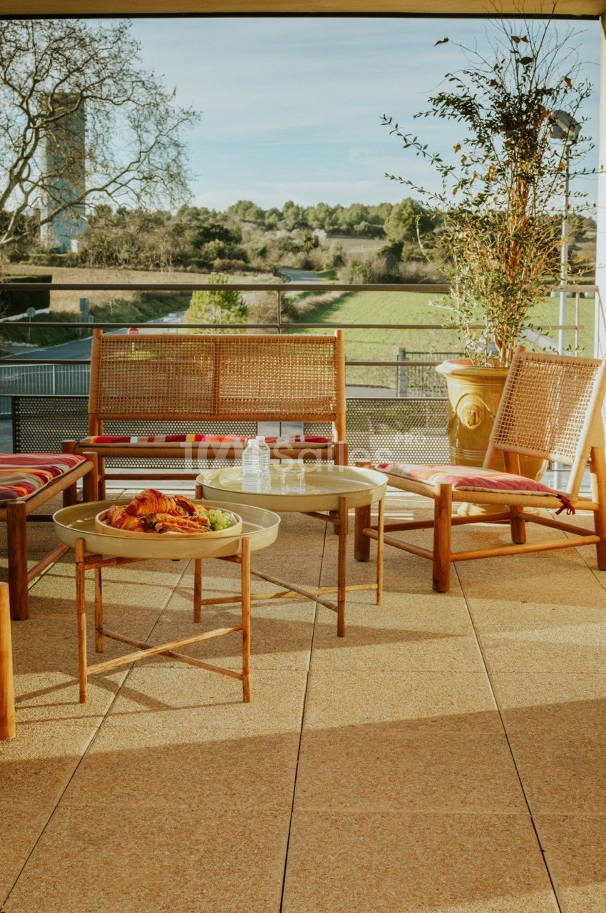 Terrasse ensoleillée avec mobilier en bois, table basse et vue sur un paysage verdoyant en arrière-plan.