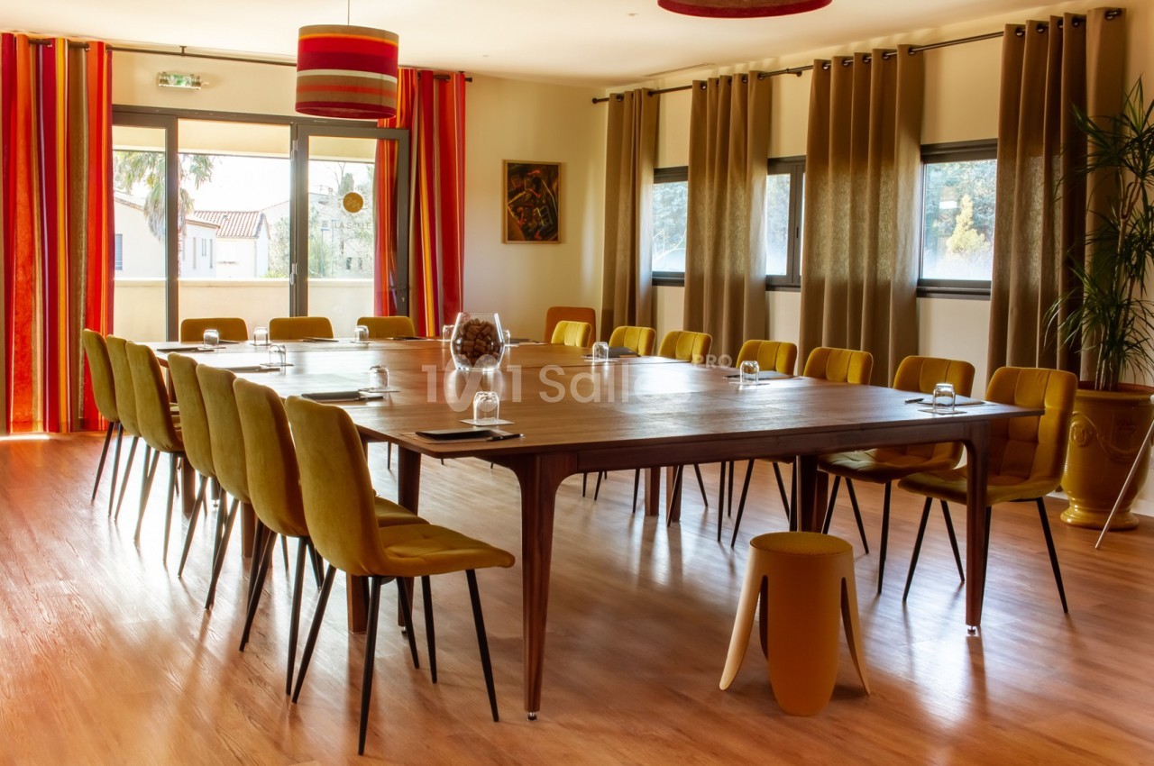 Salle de réunion lumineuse avec une grande table en bois entourée de chaises jaunes, rideaux colorés et baies vitrées.