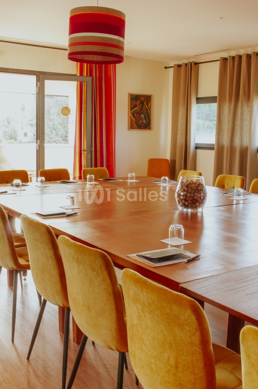 Salle de réunion lumineuse avec une grande table en bois entourée de chaises jaunes et une décoration chaleureuse.