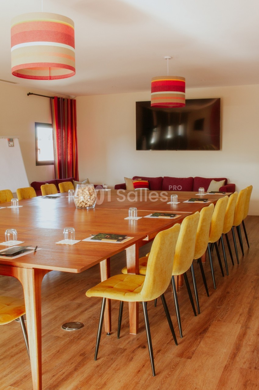 Salle de réunion lumineuse avec une grande table en bois, chaises jaunes, écran mural et décorations modernes.