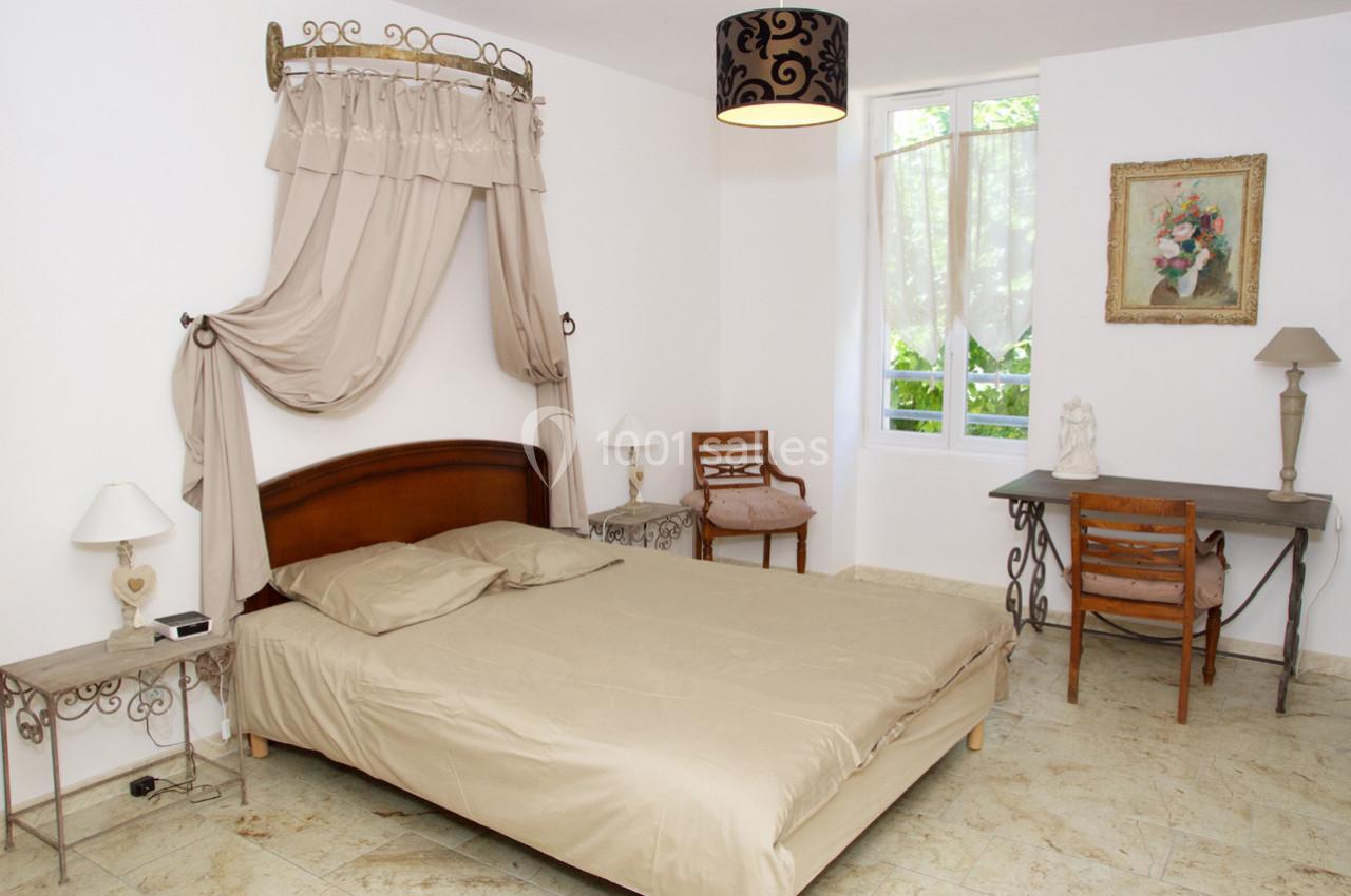 Chambre lumineuse avec un lit double, un bureau, des chaises, et une grande fenêtre donnant sur un jardin.