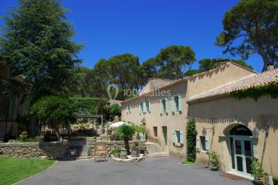 Groupe de personnes rassemblées dans une cour extérieure verdoyante devant un bâtiment en pierre avec des volets bleus.