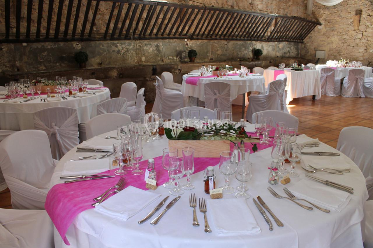 Salle de réception avec tables rondes décorées de nappes blanches et chemins de table roses, prête pour un événement.