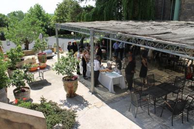Groupe de personnes rassemblées dans une cour extérieure verdoyante devant un bâtiment en pierre avec des volets bleus.